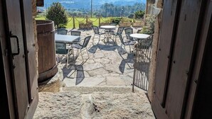 Une porte ouverte donne sur un patio extérieur doté d’un sol en pierre, de tables, de chaises et d’où l’on peut admirer une vue sur les montagnes lointaines.
