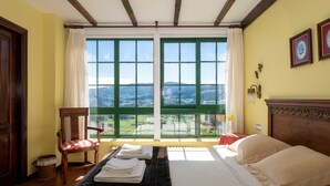 Une chambre avec un lit, une chaise, une fenêtre donnant sur les montagnes et une tête de lit en bois.