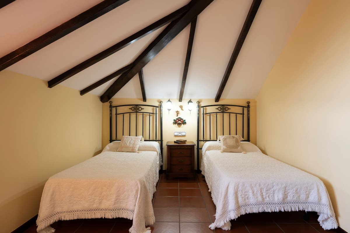 A bedroom with two beds, a nightstand, and a wall-mounted light fixture.