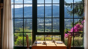 Une table à manger avec des assiettes et une tasse, placée devant une fenêtre offrant une vue sur les montagnes et la verdure.