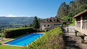 Une maison en pierre avec une piscine, entourée d’une végétation luxuriante et de collines.