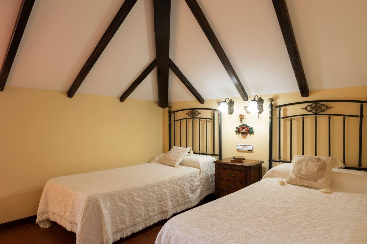 A bedroom with two single beds, wooden beams on the ceiling, and a nightstand with a lamp.