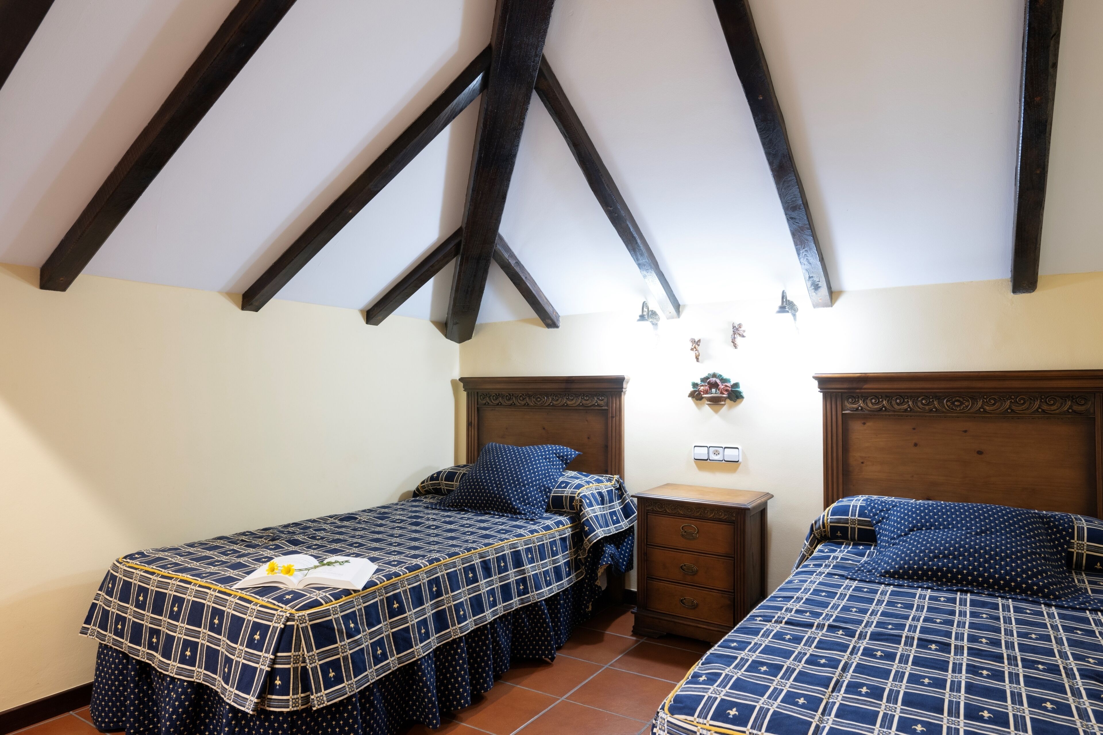 Un dormitorio con dos camas, vigas de madera en el techo y una mesita de noche con lámpara.