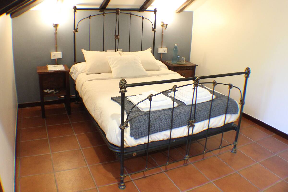 A bedroom with a four-poster bed, a nightstand, a bedside table, and a wall-mounted lamp.