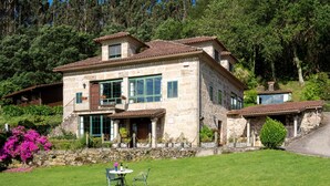 Une maison en pierre dotée d’un balcon, entourée d’une pelouse bien entretenue et d’arbres.