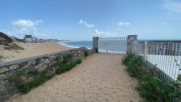 A sandy pathway leading to a beach with a white gate, a stone wall, and a fence with greenery and flowers. - Batz-sur-Mer: Duplex Apt 2 Bedrooms, 6 Guests, Parking (Batz-sur-Mer)