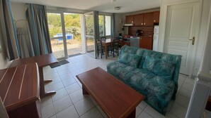 A living room with a sofa, a wooden table, and a kitchen area with cabinets and appliances. - Batz-sur-Mer: Duplex Apt 2 Bedrooms, 6 Guests, Parking (Batz-sur-Mer)