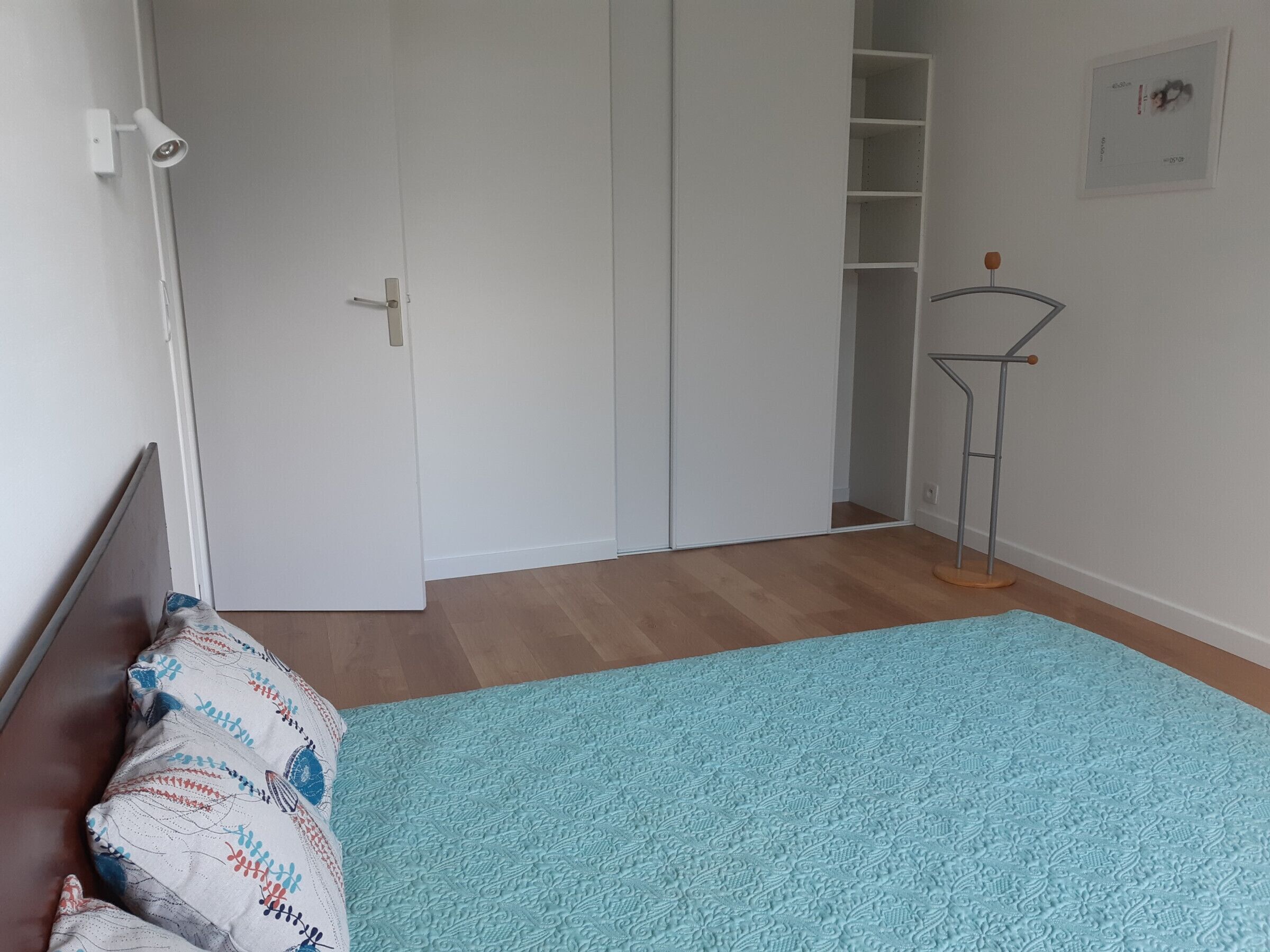 A bedroom with a bed, a wardrobe, a shelf unit, and a radiator.