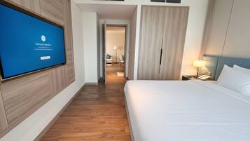 A hotel room with a bed, a TV mounted on the wall, a wardrobe, and a bedside table with a lamp.