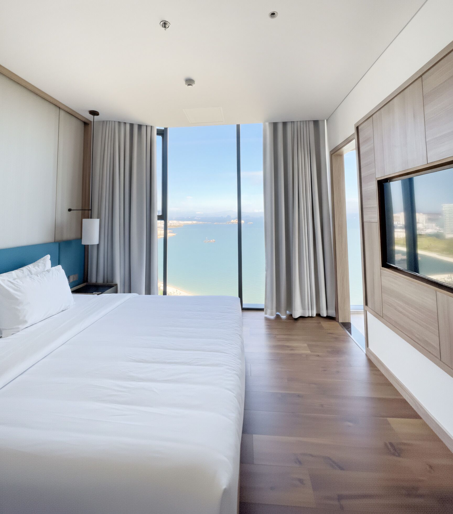 Et moderne hotelværelse med en stor seng, et fjernsyn på væggen og havudsigt.