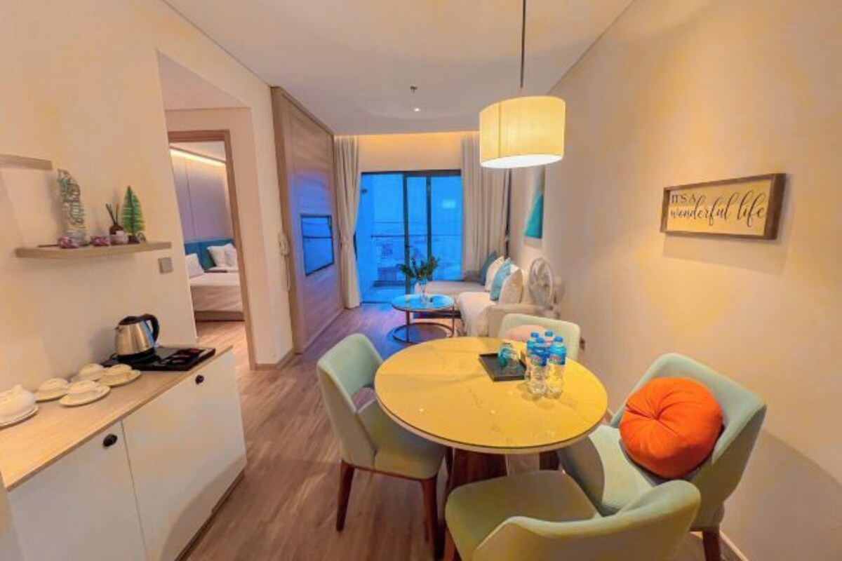 A modern hotel room with a dining area, a kitchen, and a view of the city.