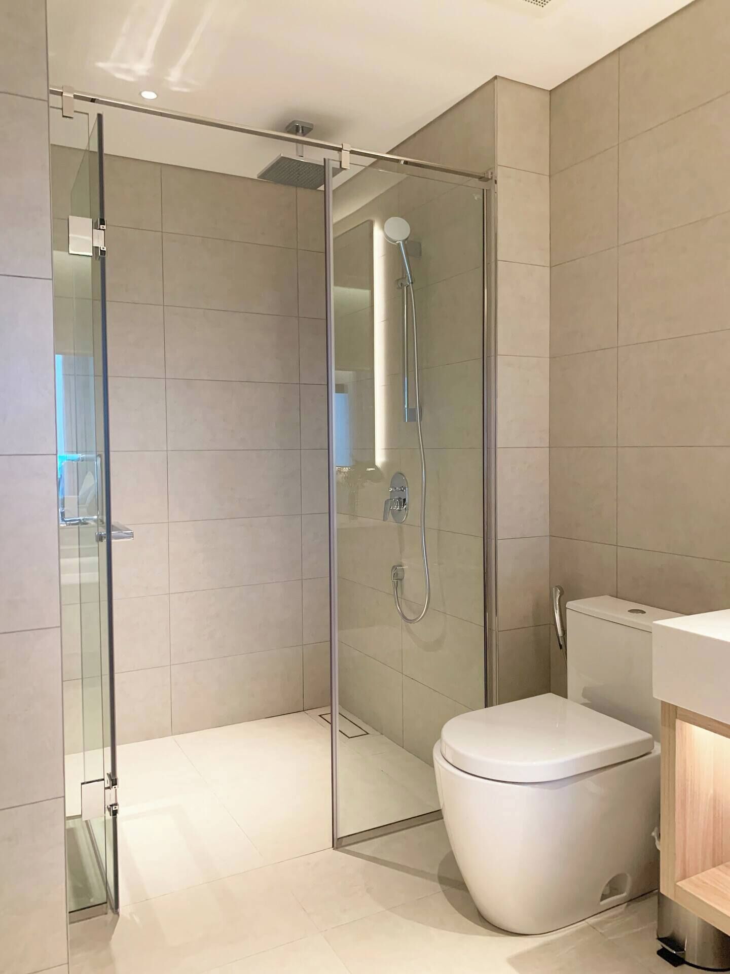 A modern bathroom with a glass-enclosed shower, a white toilet, and a wooden vanity.