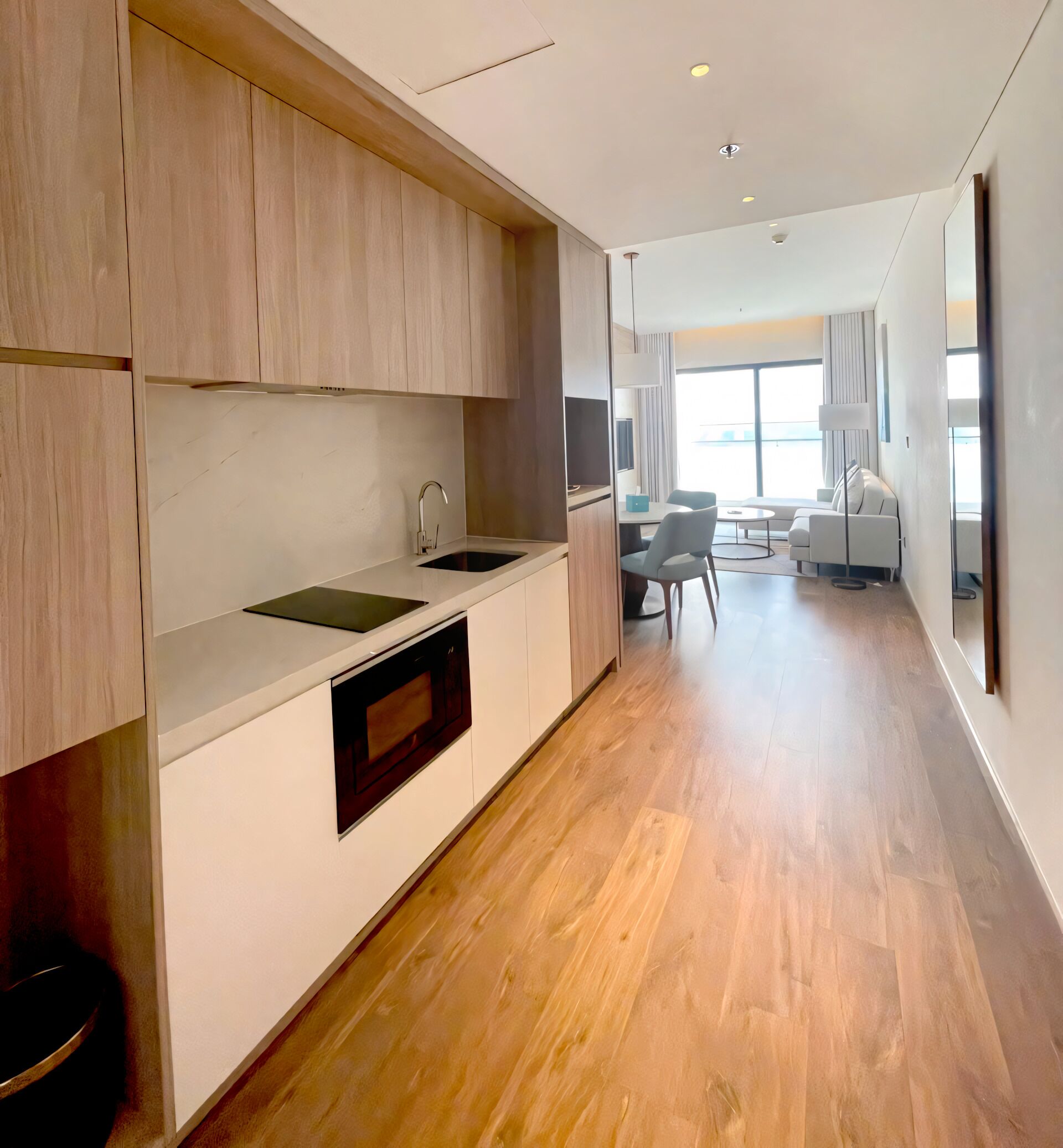 A modern kitchen with wooden cabinets, a built-in oven, and a sink. There is a dining area with a table and chairs in the background.