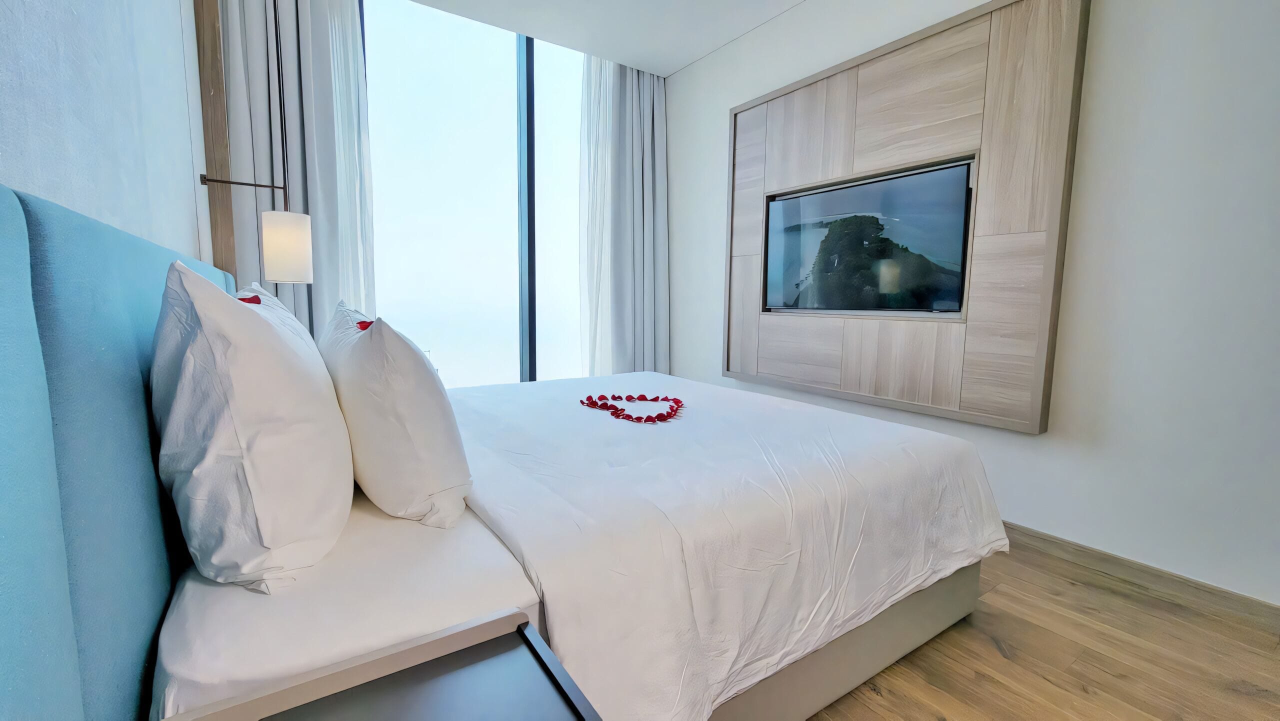 Una habitación de hotel moderna con una cama, un televisor montado en la pared y un ventanal con cortinas.