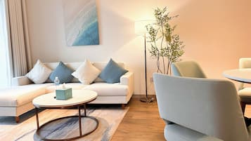 Ein modernes Wohnzimmer mit einem weißen Sofa, blauen und weißen Kissen, einem runden Couchtisch, einer Stehlampe und einer Topfpflanze.