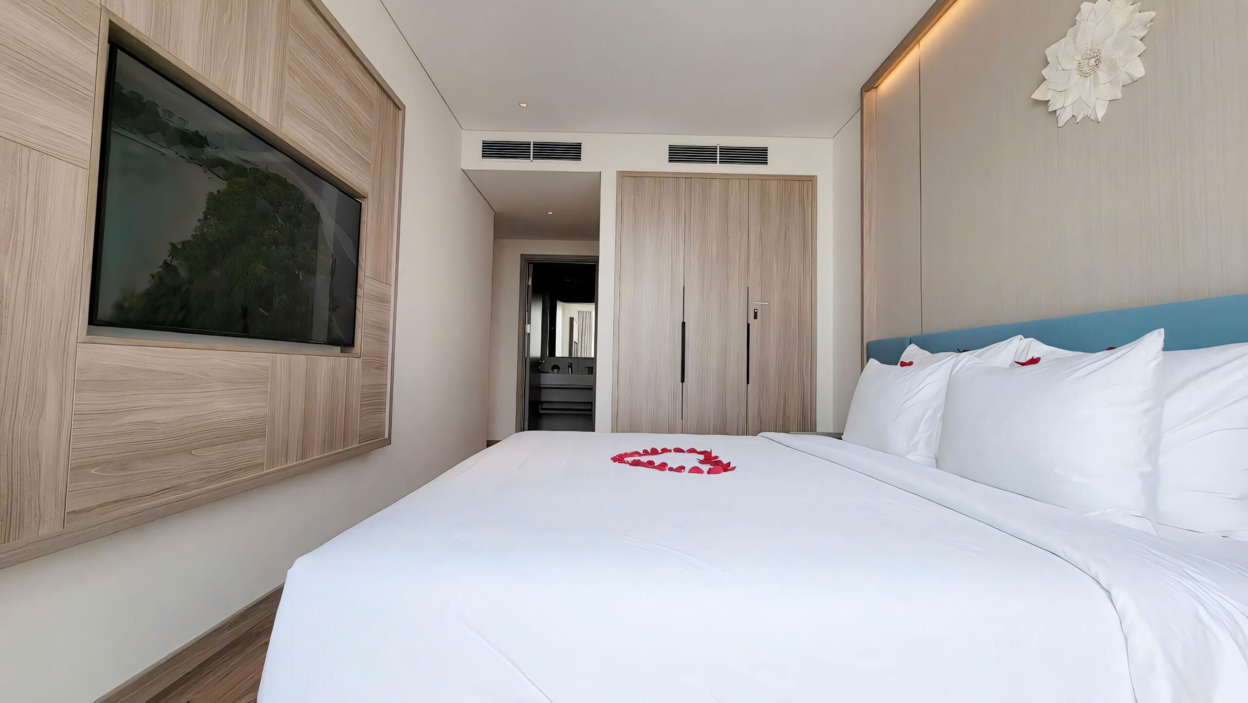 A modern hotel room with a large bed, a mounted TV, and a wardrobe.