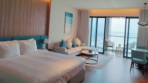 A modern hotel room with a large bed, a sofa, a coffee table, and a balcony with a view. - HB serviced Apartment - Ha Long (Bai Chay)