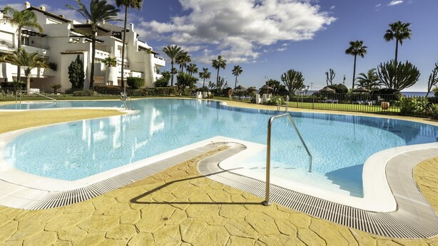 A swimming pool with a clear blue sky and palm trees in the background. - Luxury beachfront apartment in Estepona (Estepona)