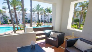 A sunlit patio with wicker furniture, a pool view, and a white building in the background. - Spacious Apartment in Estepona with WiFi and Parking (Estepona)