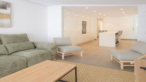 Una sala de estar moderna con un sofá, sillones, una mesa de centro y una cocina al fondo.