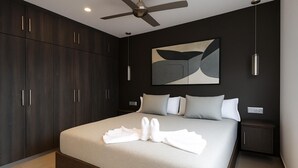 Una habitación de hotel moderna con una cama grande, un armario de madera oscura y un ventilador de techo.