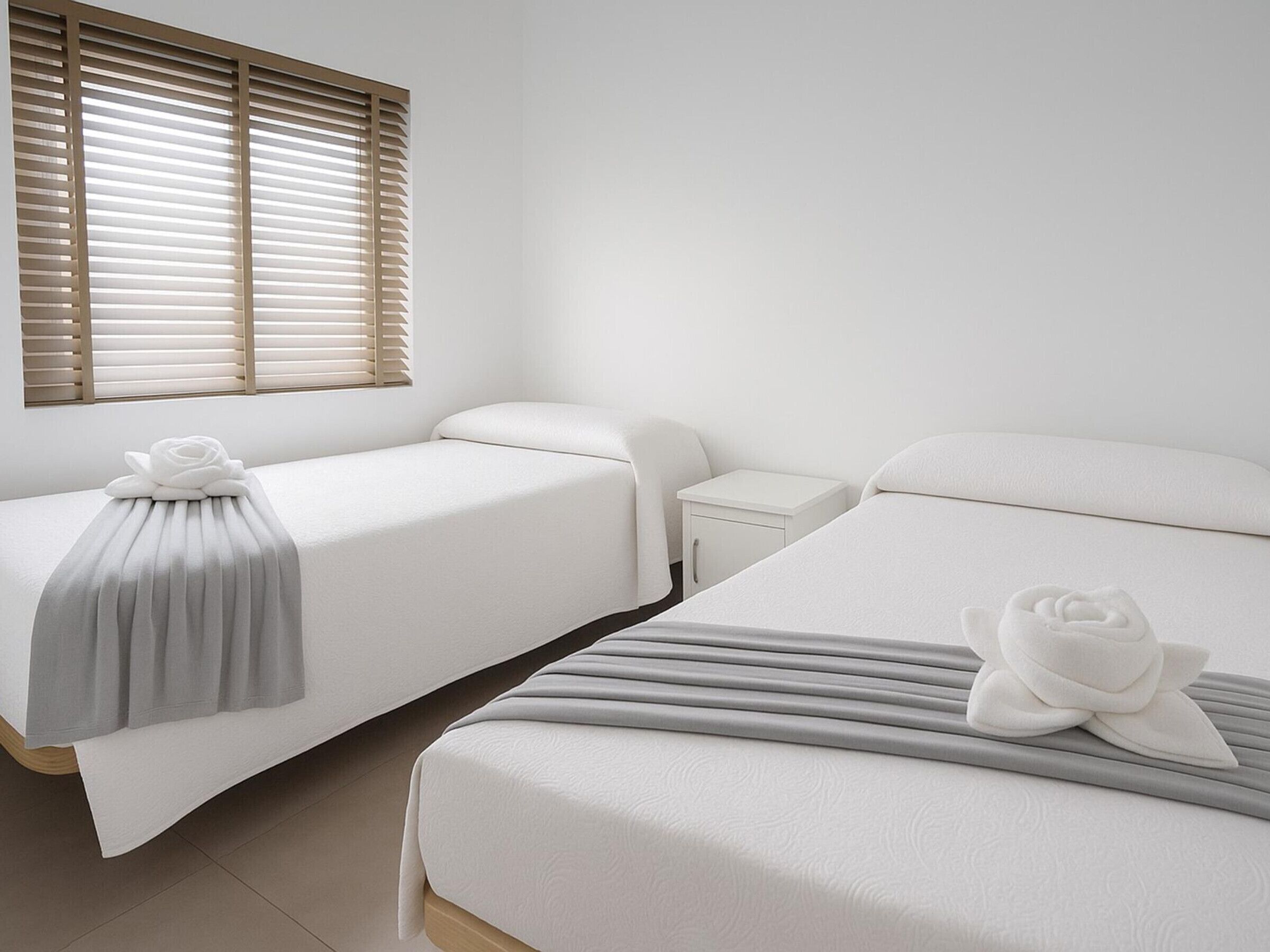 A hotel room with two beds, a nightstand, and a window with blinds.
