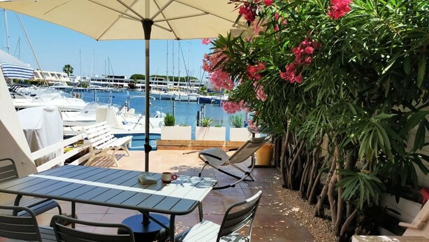 An outdoor patio with a table and chairs, a large umbrella, and a view of a marina with boats.