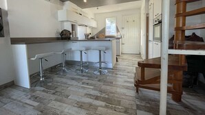 A modern kitchen with a central island, bar stools, and a wooden staircase.