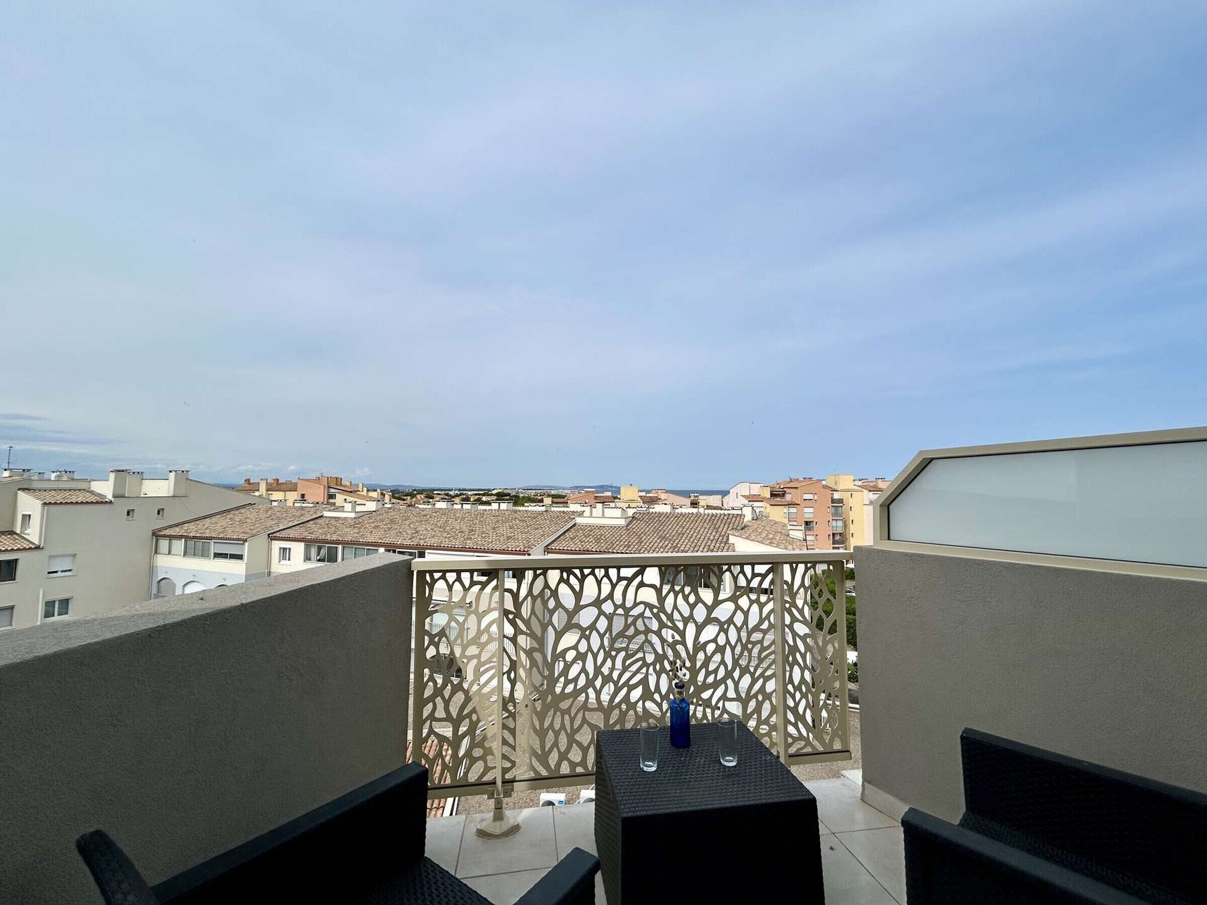 A balcony with a view of a residential area, a table with chairs, and a decorative screen.