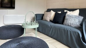 A modern living room with a grey sofa, black and white cushions, a small side table with glasses, and a mounted TV. - Cozy Montgenèvre apartment, 4 pers, near center (Montgenèvre)