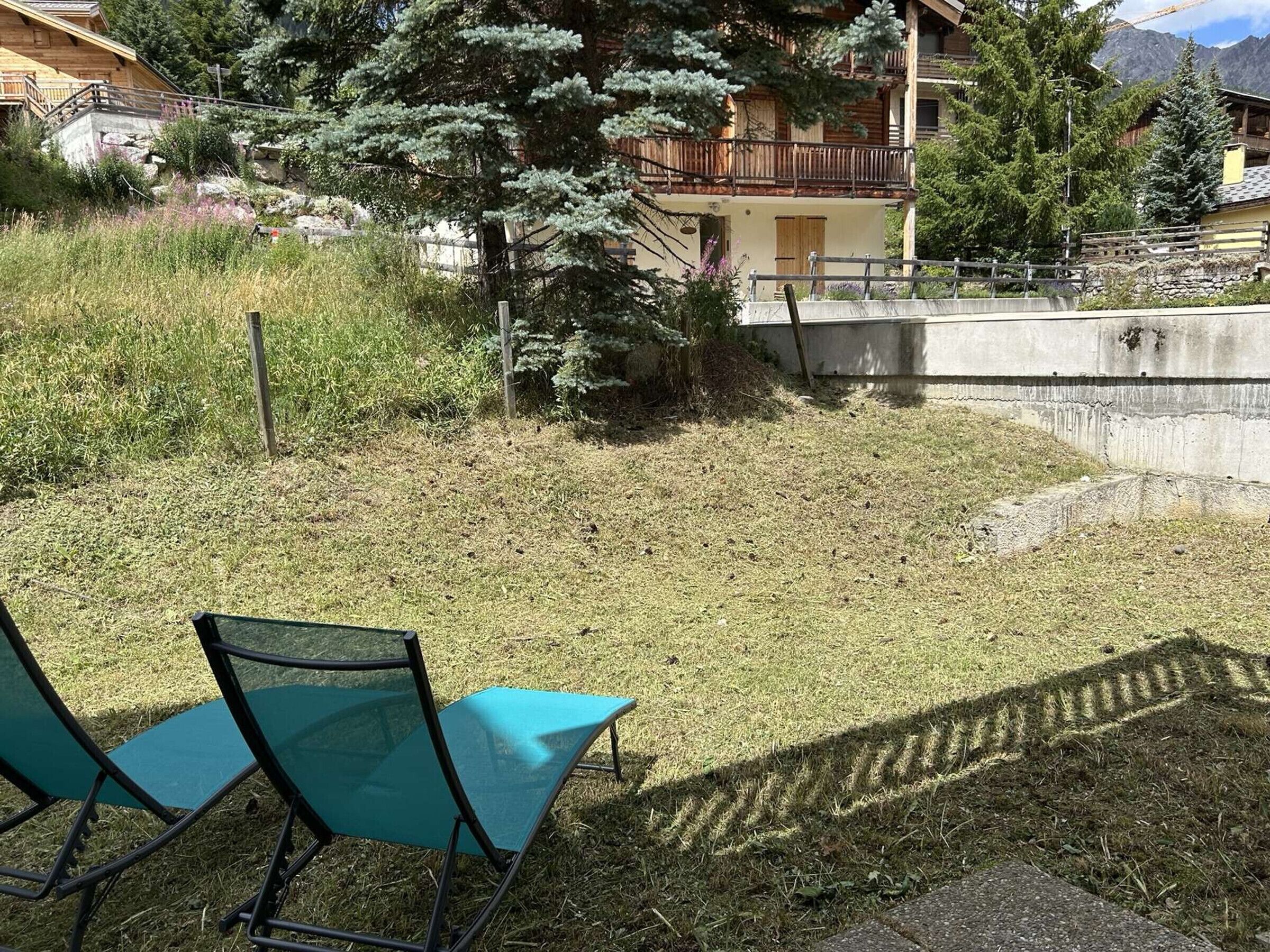 A grassy outdoor area with two green chairs and a concrete wall.