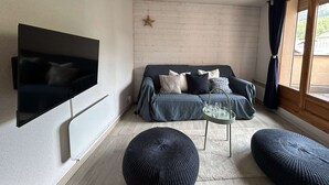 A living room with a flat-screen TV, a sofa with cushions, a coffee table, and two ottomans. - Cozy Montgenèvre apartment, 4 pers, near center (Montgenèvre)