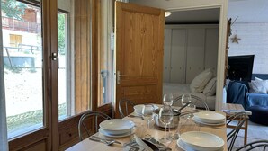 A dining area with a wooden table set for four, chairs, and a view of the outdoors through a sliding door. - Cozy Montgenèvre apartment, 4 pers, near center (Montgenèvre)