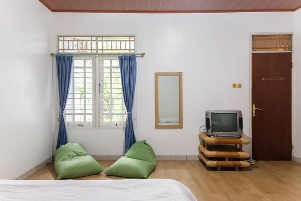 A room with a bed, two green pillows, a television on a wooden stand, a mirror, and a door. - Calma Villa at Cipanas Bogor (Cipanas)