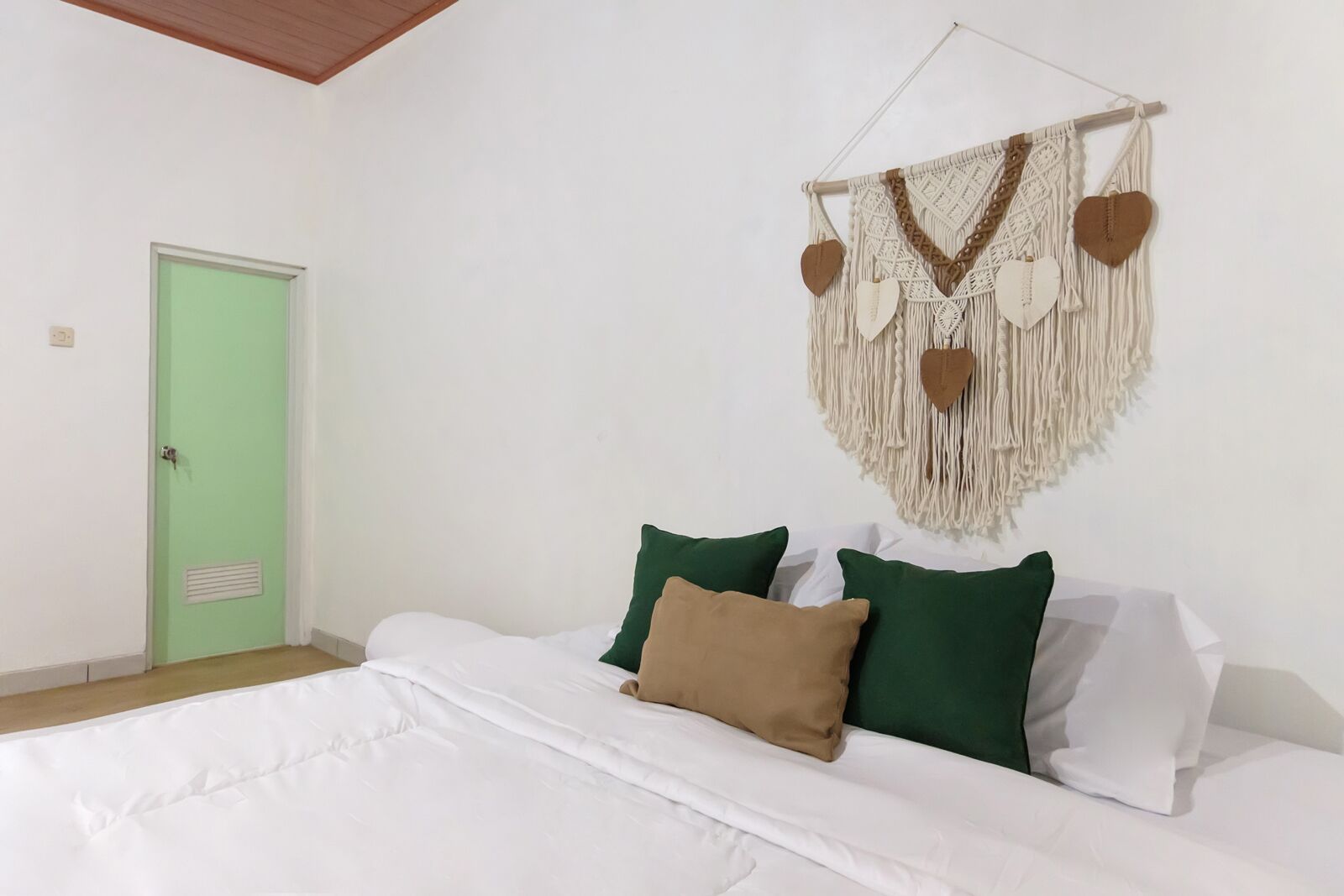 A bedroom with a bed, green and white pillows, a macrame wall hanging, and a green door.