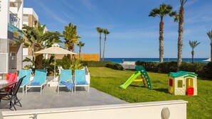 Un espace aménagé au bord de la piscine, avec des chaises longues, une aire de jeux pour enfants et des palmiers.