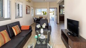 A living room with a sofa, coffee table, TV, and a dining area with chairs and a table. - A modern 2 bedroom house in the absolute heart of Protaras with fantastic views of the sea (Protaras)