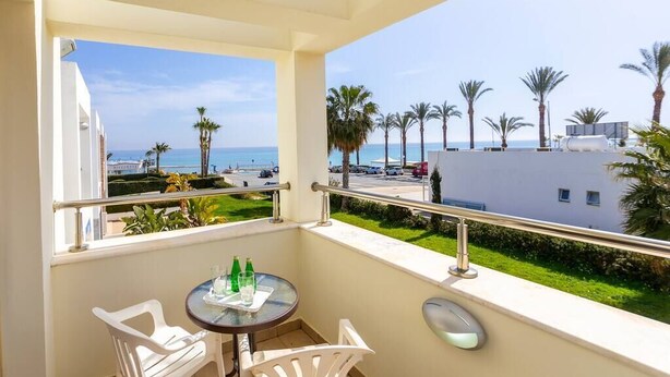 A balcony with a table and chairs, overlooking a beach and palm trees. - A modern 2 bedroom house in the absolute heart of Protaras with fantastic views of the sea (Protaras)