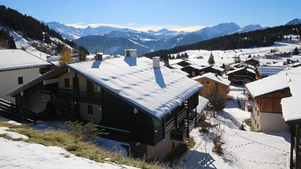 A snow-covered mountain village with traditional wooden houses and a clear view of the surrounding peaks.