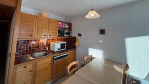 A compact kitchen with wooden cabinets, a microwave, a sink, and a dining table with chairs.