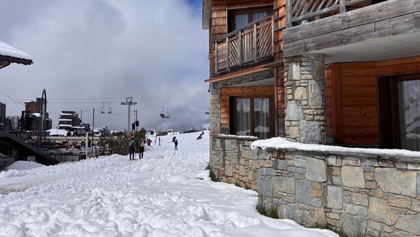 A wooden building with a stone foundation, a balcony, and a ski lift in the background.