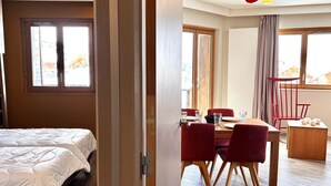 A hotel room with a bed, a dining area with a table and chairs, and large windows.