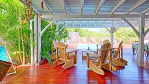 Eine überdachte Terrasse im Freien mit Holzmöbeln, einem Pool und üppiger Bepflanzung.