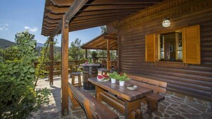 A wooden cabin with a stone patio, wooden benches, a table with plates and a bottle, and a barrel. - Three charming log cabins in a gated property at the beautiful Troodos mountain (Spilia)