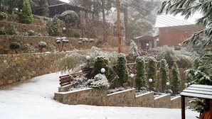 A snow-covered outdoor area with stone walls, a wooden bench, and snow-laden trees. - Three charming log cabins in a gated property at the beautiful Troodos mountain (Spilia)