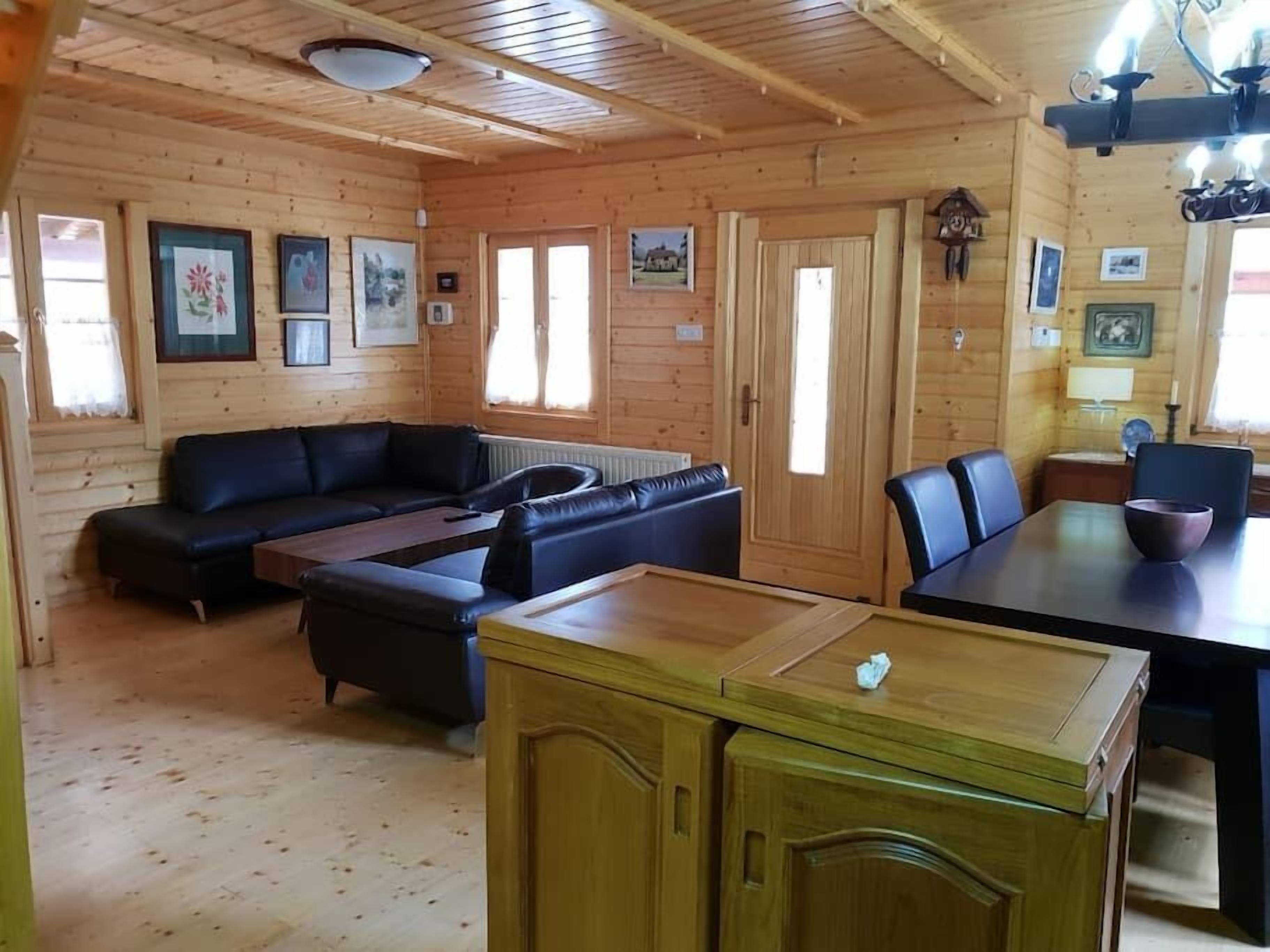 A wooden cabin interior with a sofa, dining table, and kitchen area.