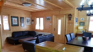 A wooden cabin interior with a sofa, dining table, and kitchen area. - Three charming log cabins in a gated property at the beautiful Troodos mountain (Spilia)