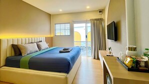 A hotel room with a bed, a desk with a flat-screen TV, a window with curtains, and a view of the outside. - Ti amo Kohlarn (Koh Lan)