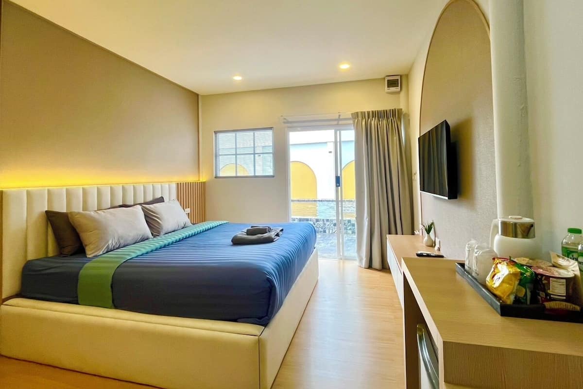 Quarto de hotel com cama, escrivaninha com TV de tela plana, janela com cortinas e vista para o exterior.