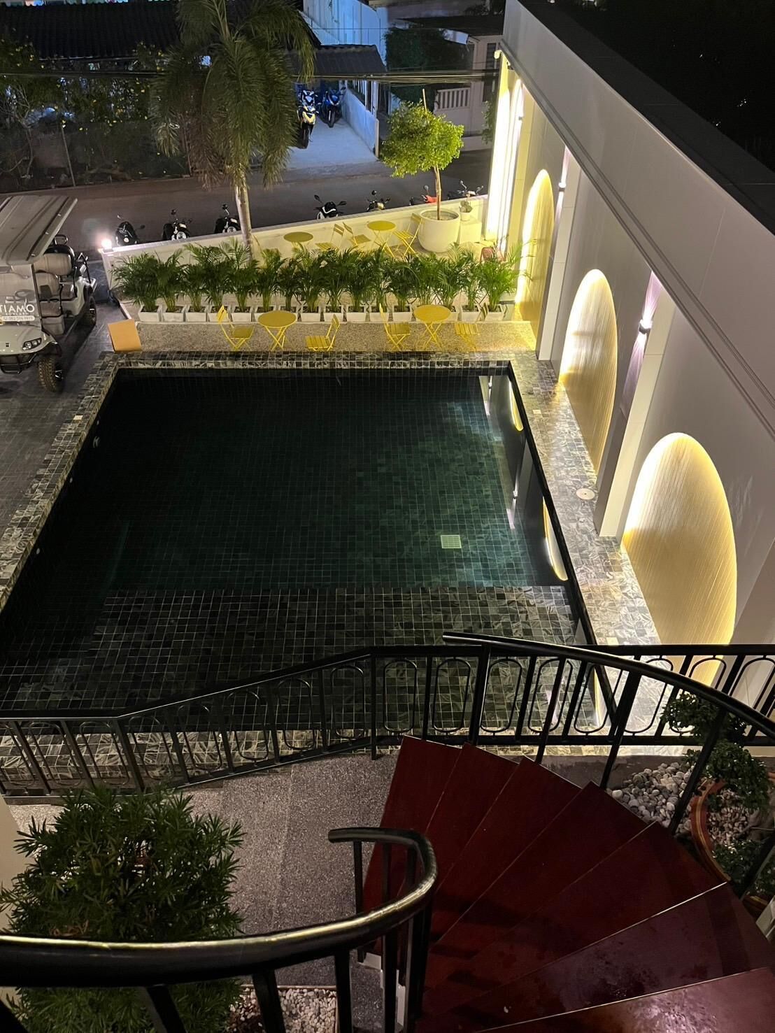 A rooftop pool with a tiled floor, surrounded by a railing and potted plants.